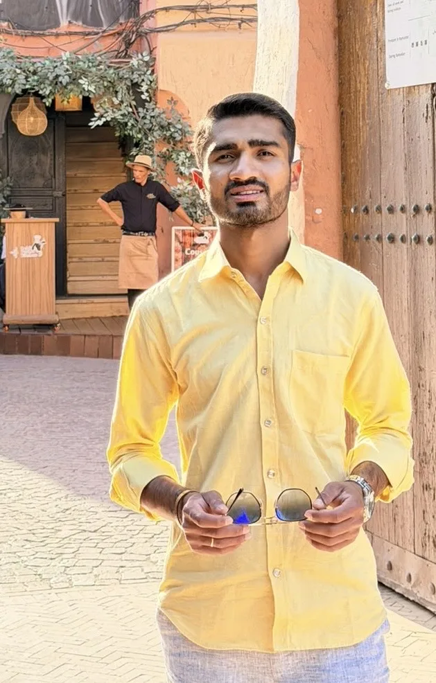 Arnavut kaldırımlı bir meydanda sarı gömlekli Om Gauswami