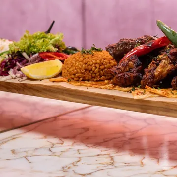 A long board of grilled meats with dips